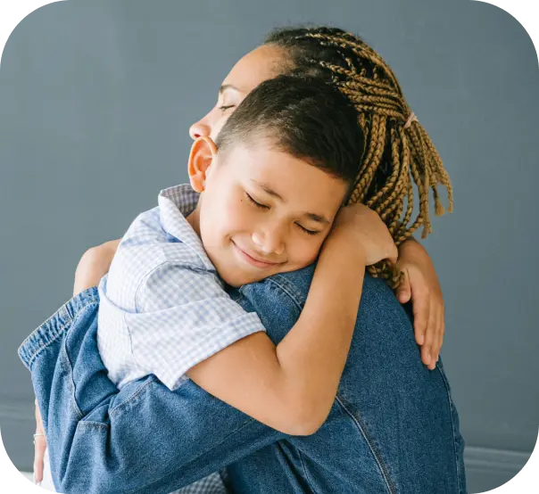 A smiling boy with his eyes closed, hugging a grown-up